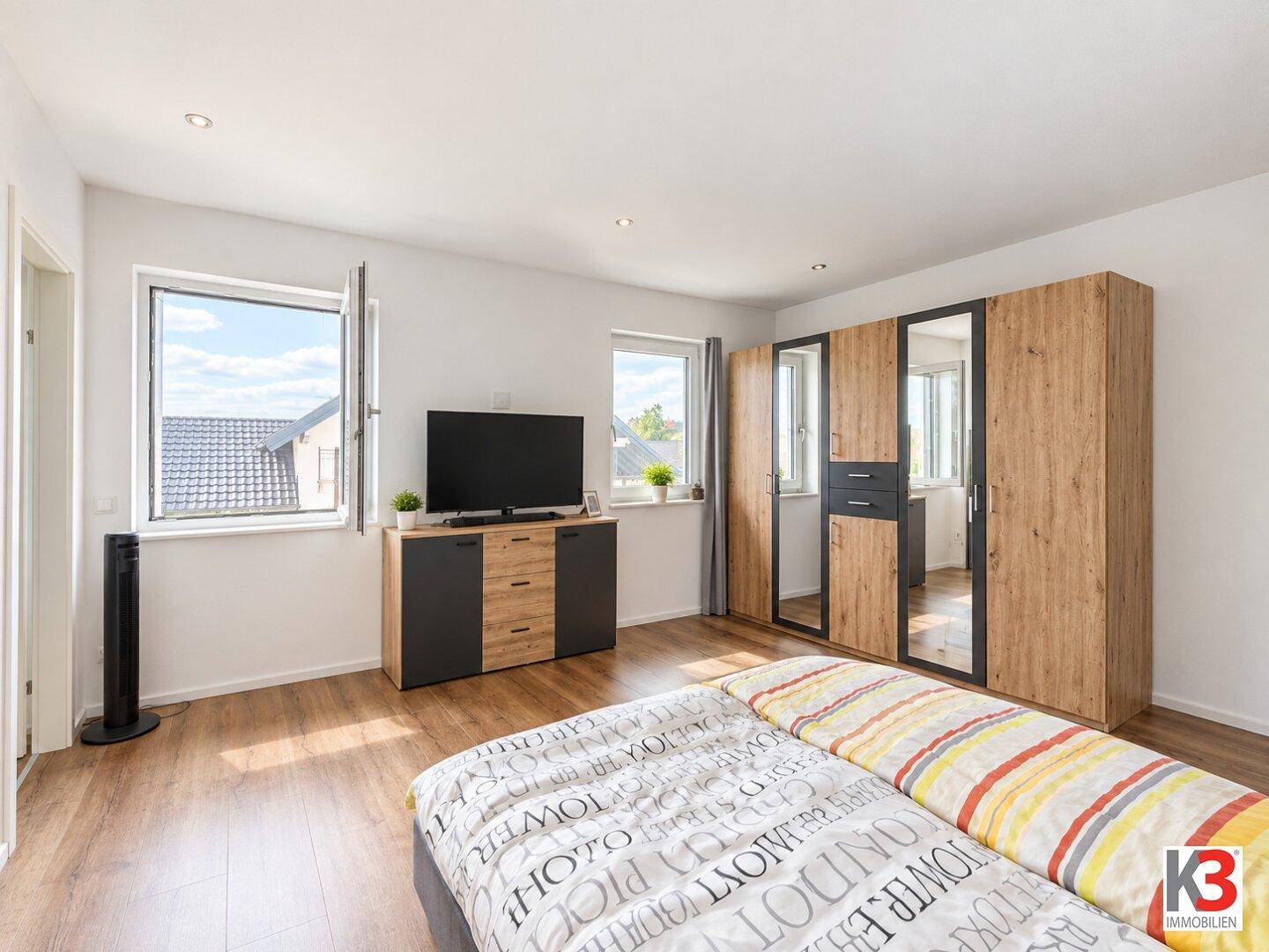 Geräumiges Schlafzimmer mit Holzboden, großen Fenstern und modernem Kleiderschrank.