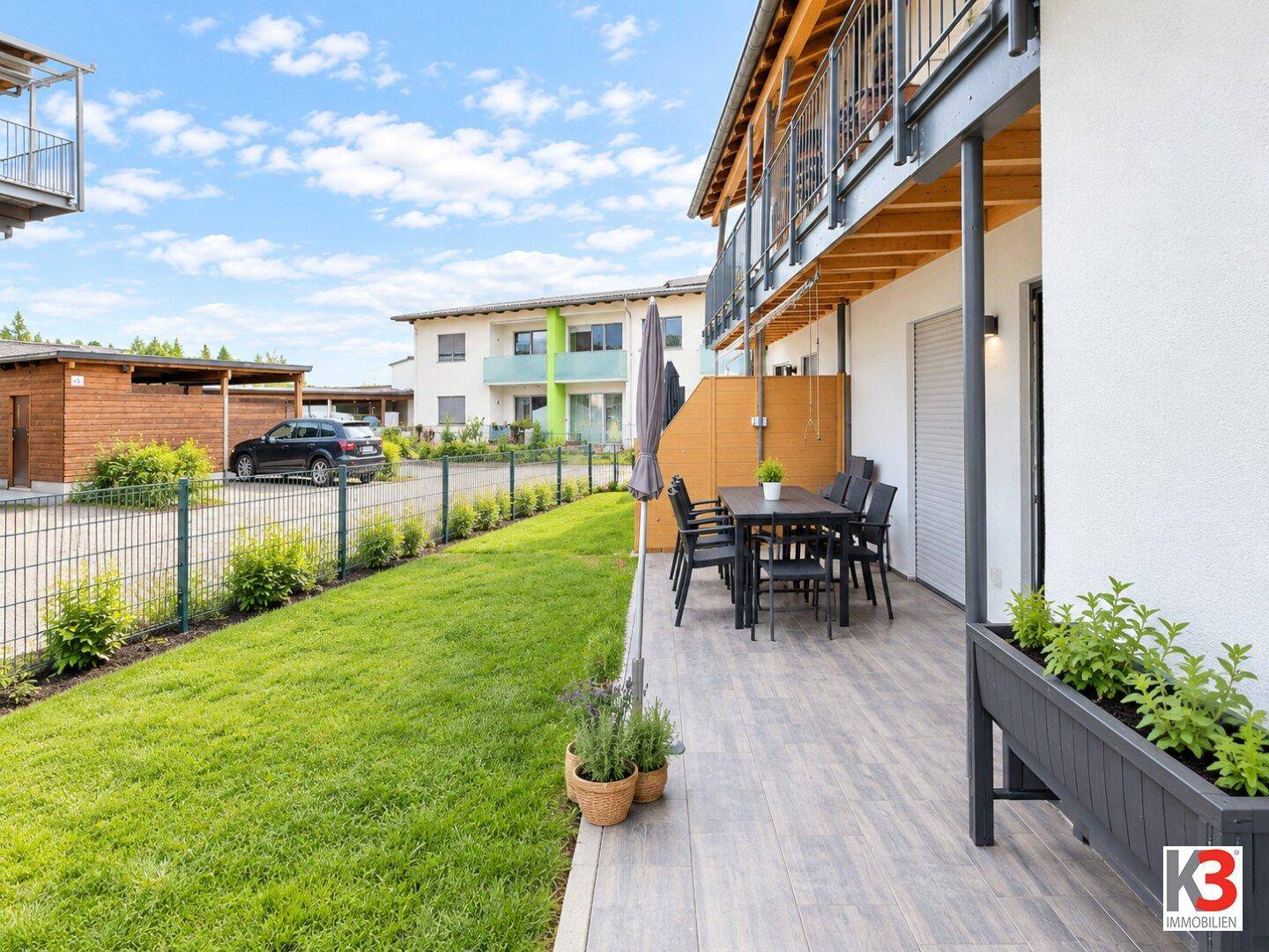 Sonniger Terrassenbereich mit Gartenmöbeln, Rasenfläche und Blick auf die Umgebung.