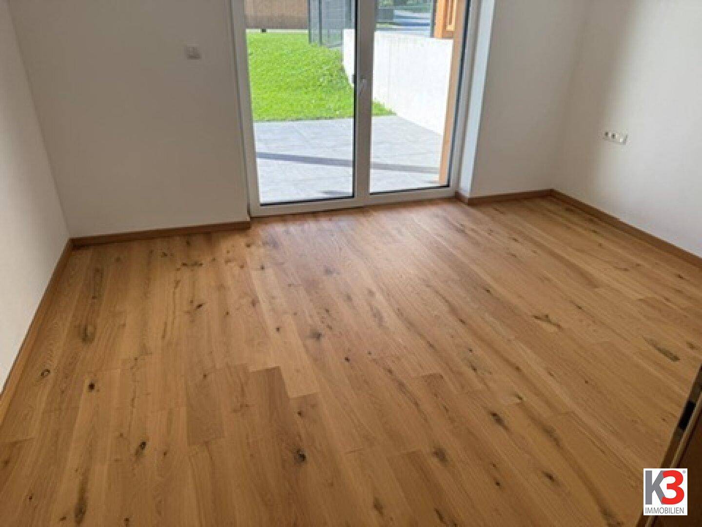 Lichtdurchflutetes Zimmer mit Holzboden und Schiebetür zum Außenbereich.