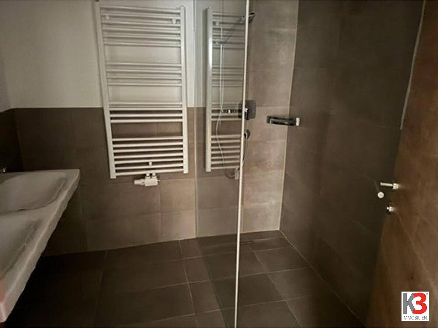 Geräumiges Badezimmer mit ebenerdiger Dusche, Fliesen und Handtuchheizkörper.
