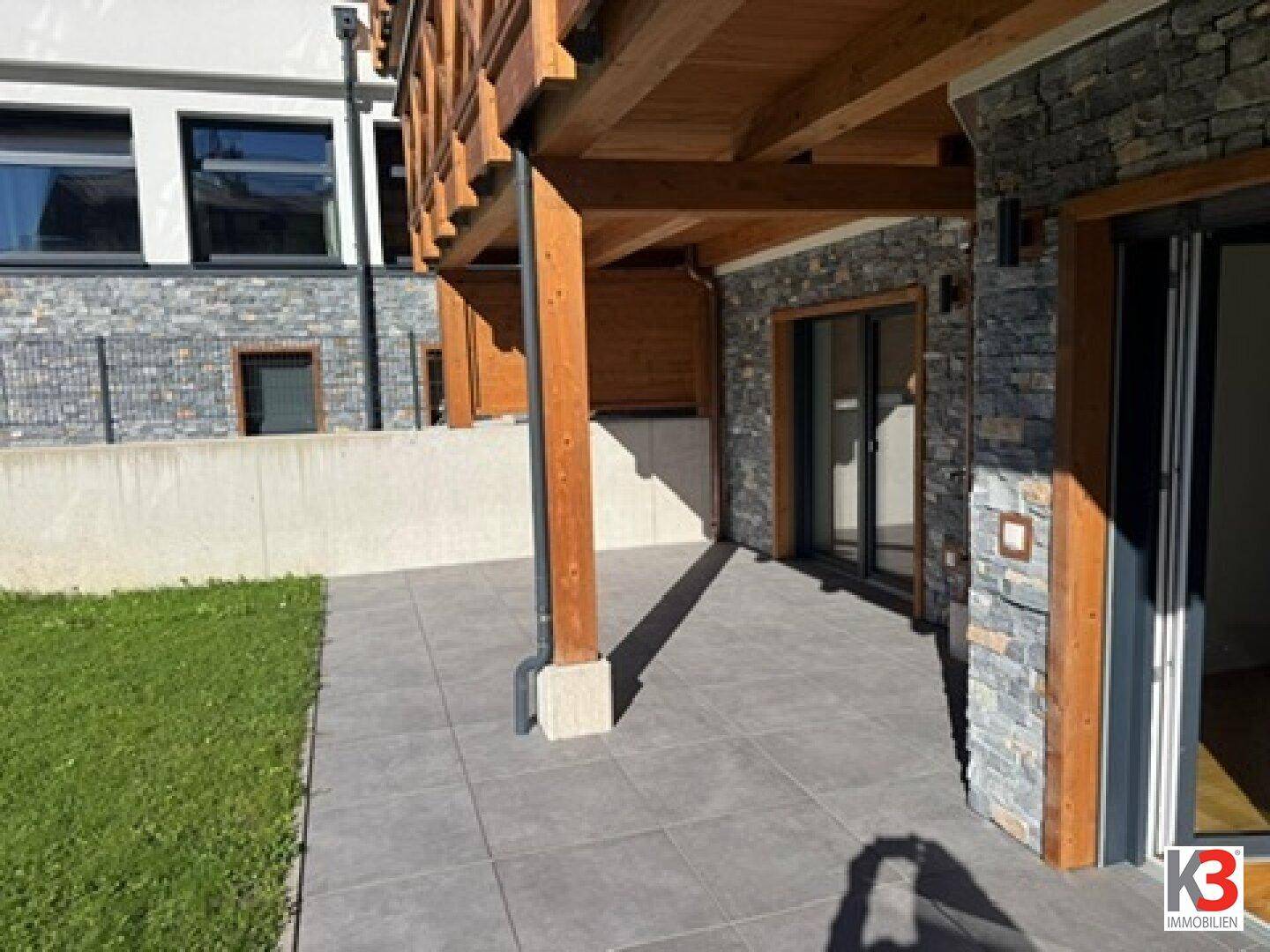 Gepflasterte Terrasse mit Steinverkleidung und Holzelementen am Gebäude.