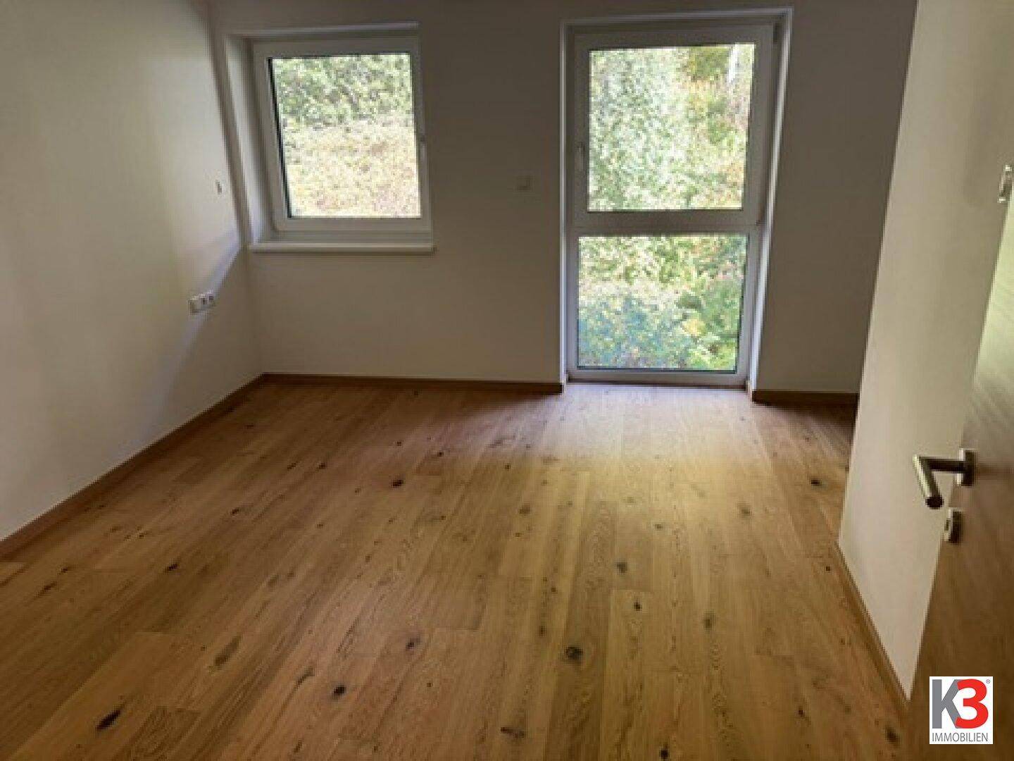 Geräumiges Schlafzimmer mit Holzboden und zwei Fenstern für viel Tageslicht.