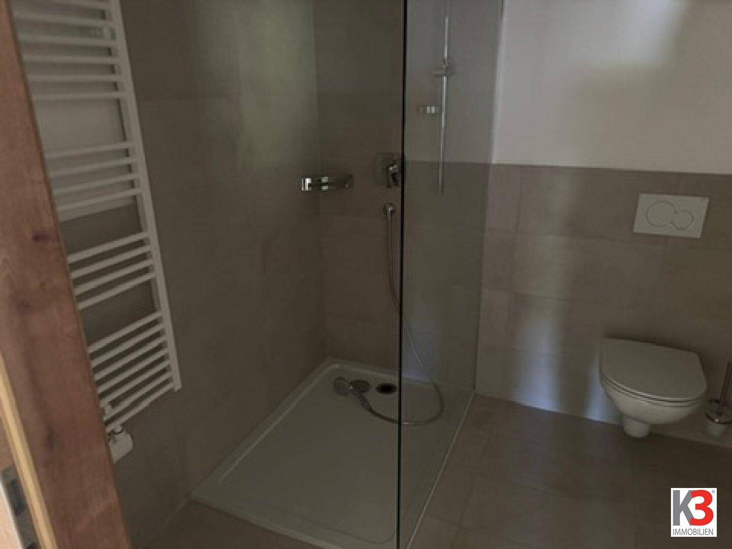 Modernes Badezimmer mit ebenerdiger Dusche, beheiztem Handtuchhalter und Wand-WC.