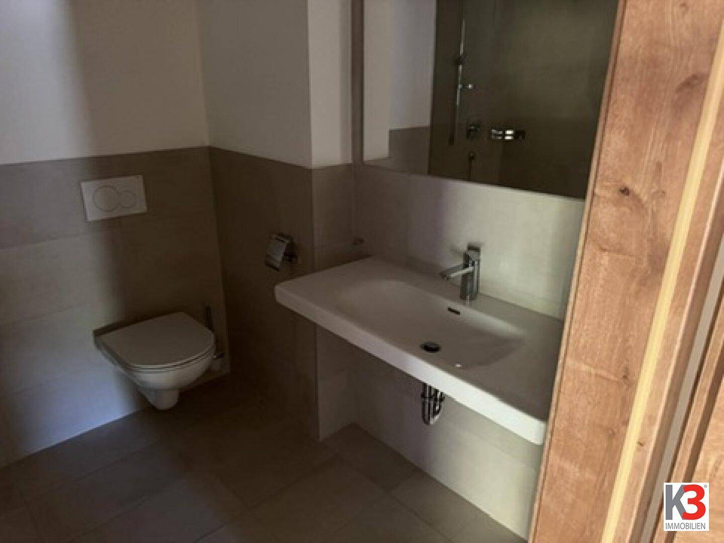 Modernes Badezimmer mit Wand-WC, Waschbecken und großem Spiegel.