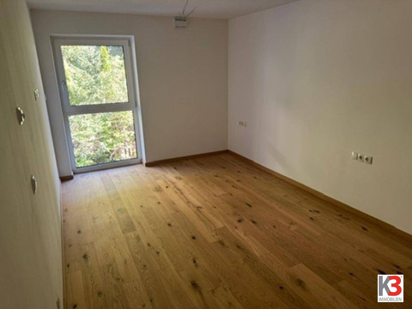 Ruhiges Schlafzimmer mit Holzboden und großem Fenster mit Blick ins Grüne.