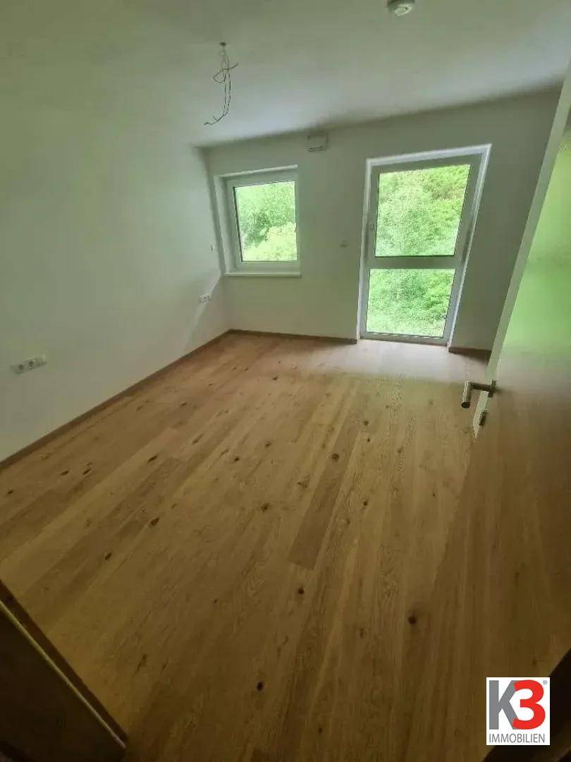 Helles Schlafzimmer mit Holzboden und Zugang zu einem Balkon oder einer kleinen Terrasse.