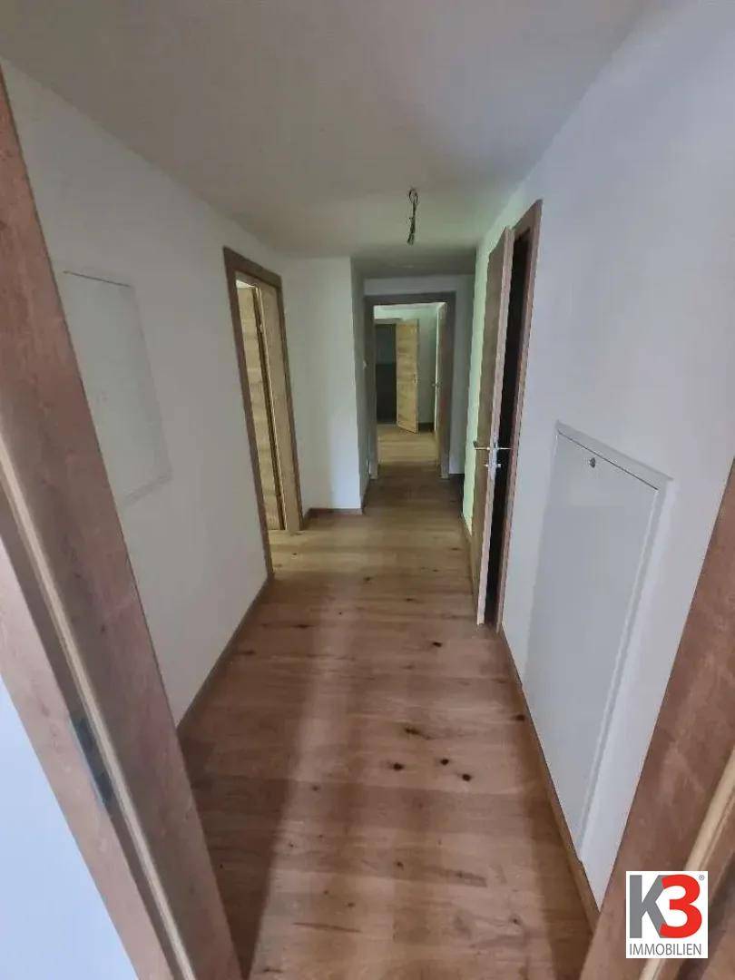 Langer, heller Flur mit Holzboden und mehreren Türen zu den Zimmern.