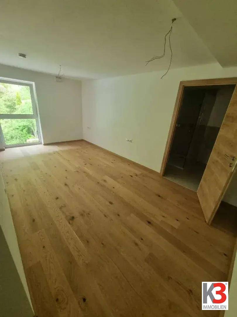 Leeres Zimmer mit Holzboden und Fenster, das viel natürliches Licht hereinlässt.