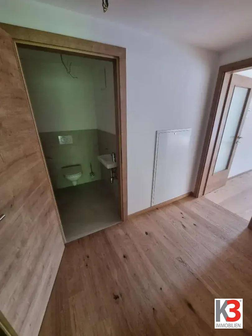 Heller Flur mit Holzboden und Zugang zu einem Gäste-WC.
