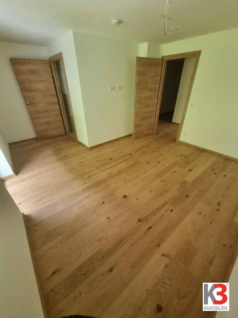 Leeres Zimmer mit Holzboden und mehreren Türen, das vielseitig nutzbar ist.