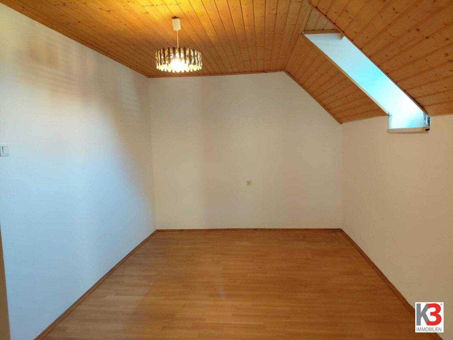 Dachgeschosszimmer mit Holzdecke, Holzboden und einem Dachfenster für zusätzliches Licht.