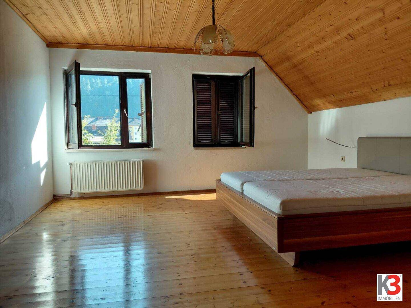 Schlafzimmer im Dachgeschoss mit Holzboden, Holzdecke und Fenstern mit Bergblick.