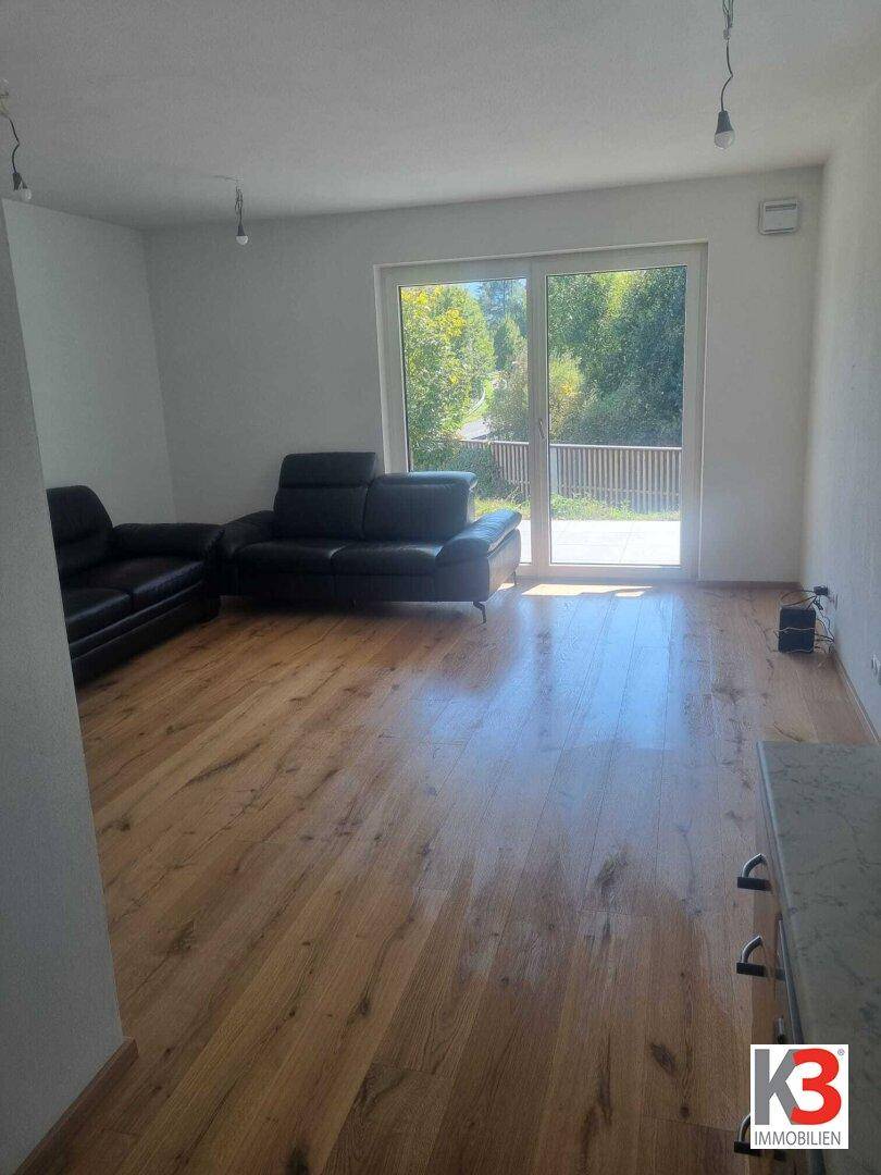 Helles Wohnzimmer mit Holzboden, zwei Sofas und Zugang zu einem Balkon mit grüner Aussicht.
