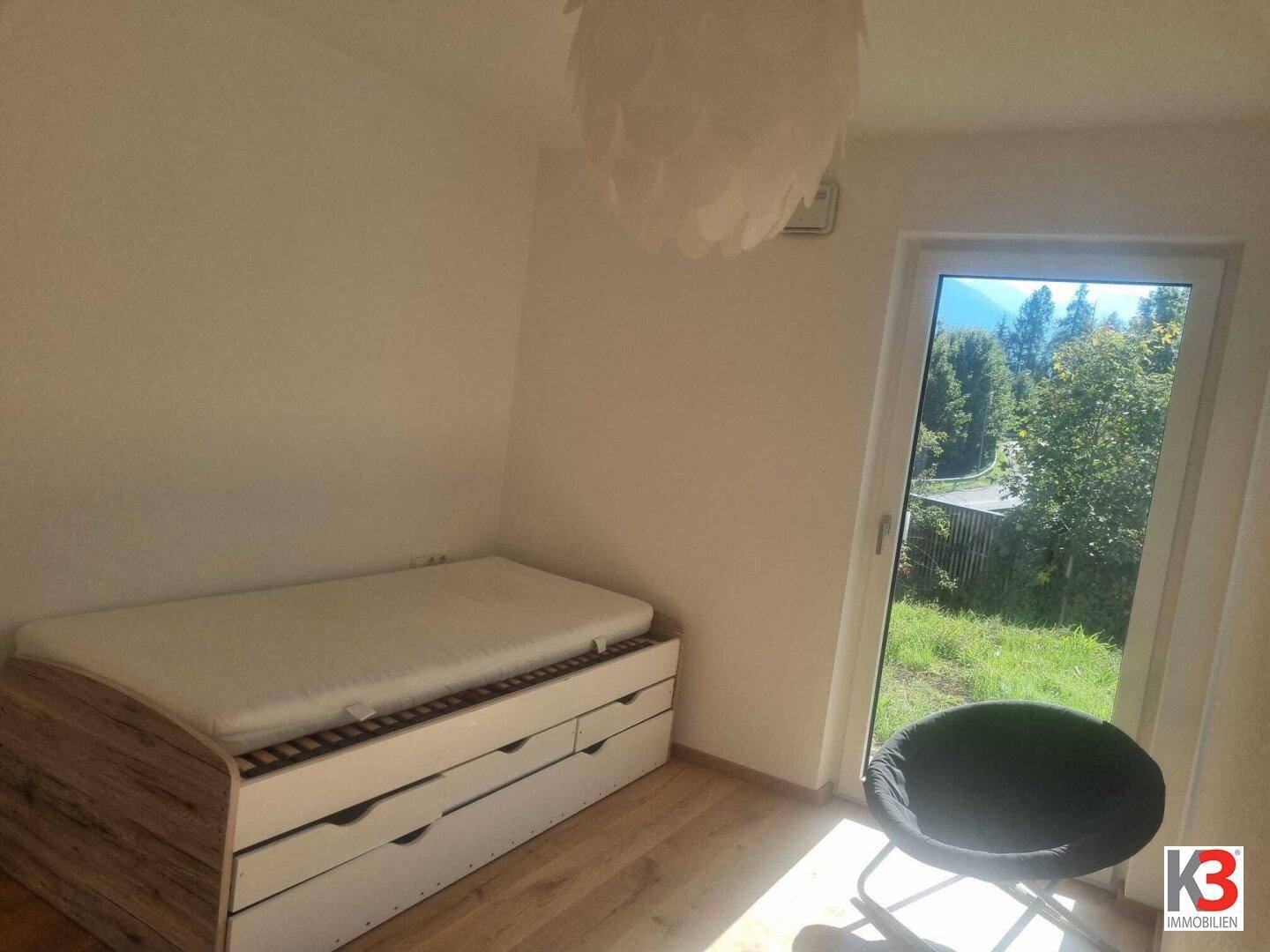 Helles Schlafzimmer mit Einzelbett, Holzboden und großem Fenster mit Blick ins Grüne.