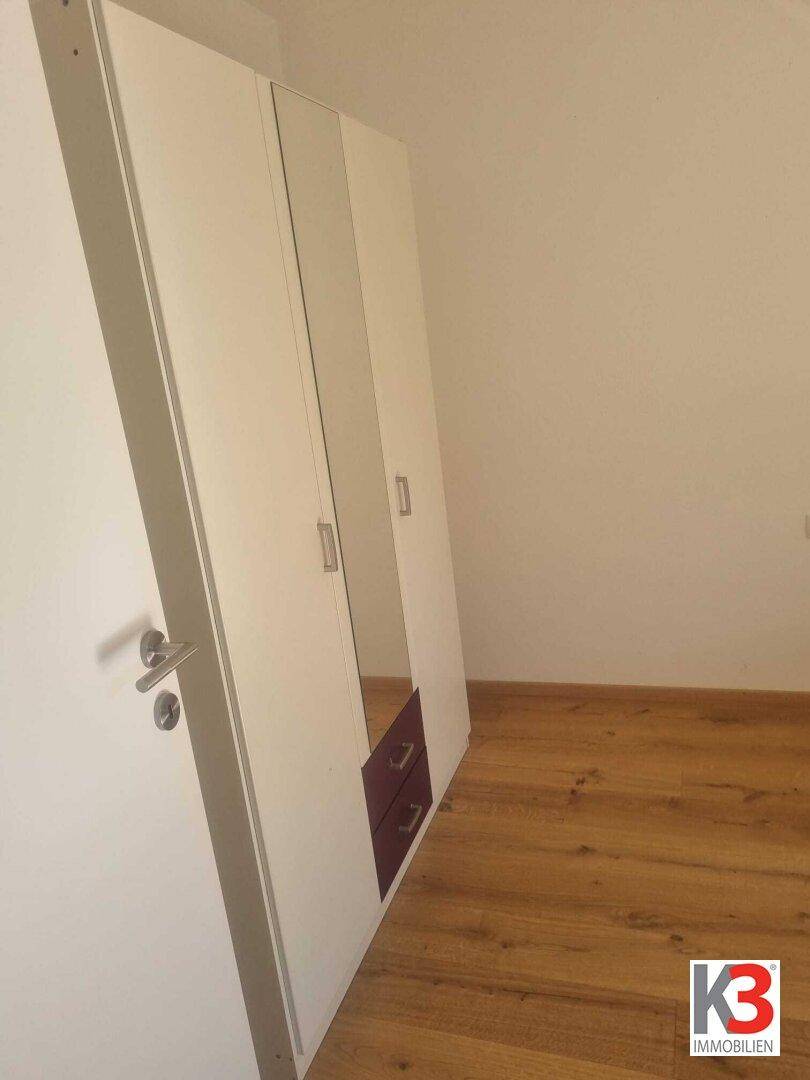 Weißer Kleiderschrank mit Spiegeltüren und Schubladen auf einem Holzboden.