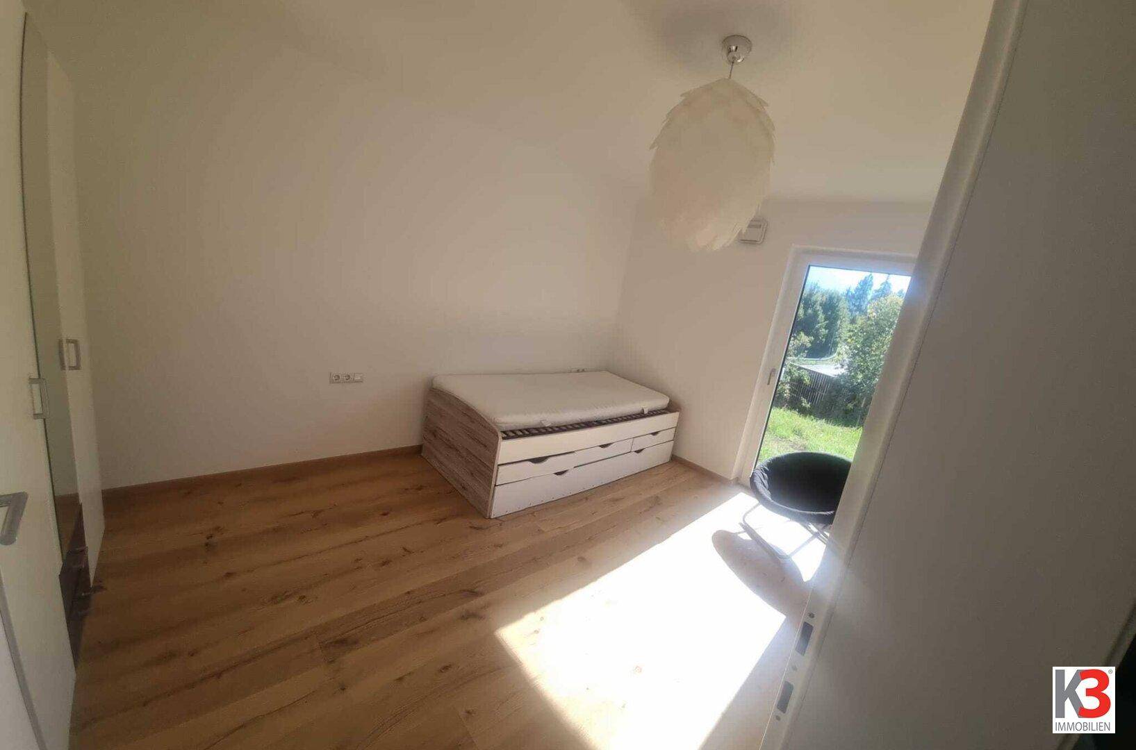 Geräumiges Schlafzimmer mit Bett, Holzboden und viel Tageslicht durch das große Fenster.