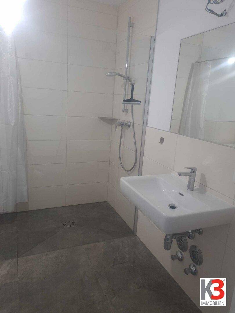 Modernes Badezimmer mit ebenerdiger Dusche, Waschbecken und hellen Fliesen.