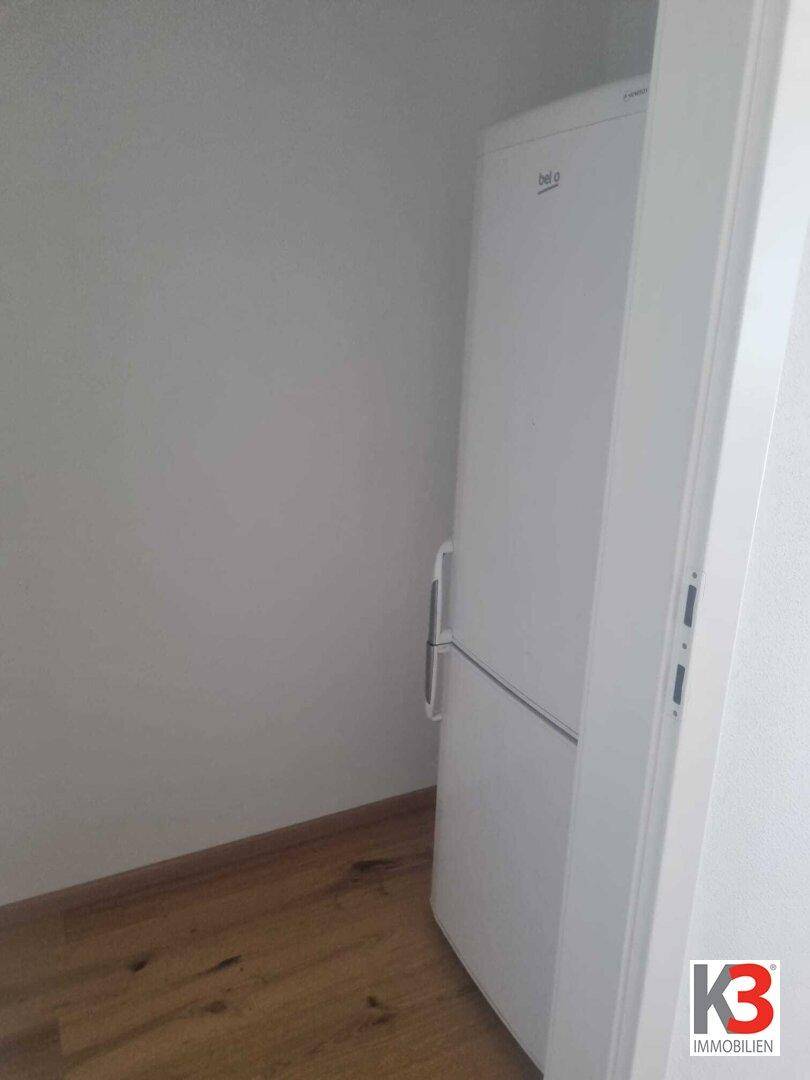 Weißer Kühlschrank in einer Ecke des Raumes mit Holzboden.