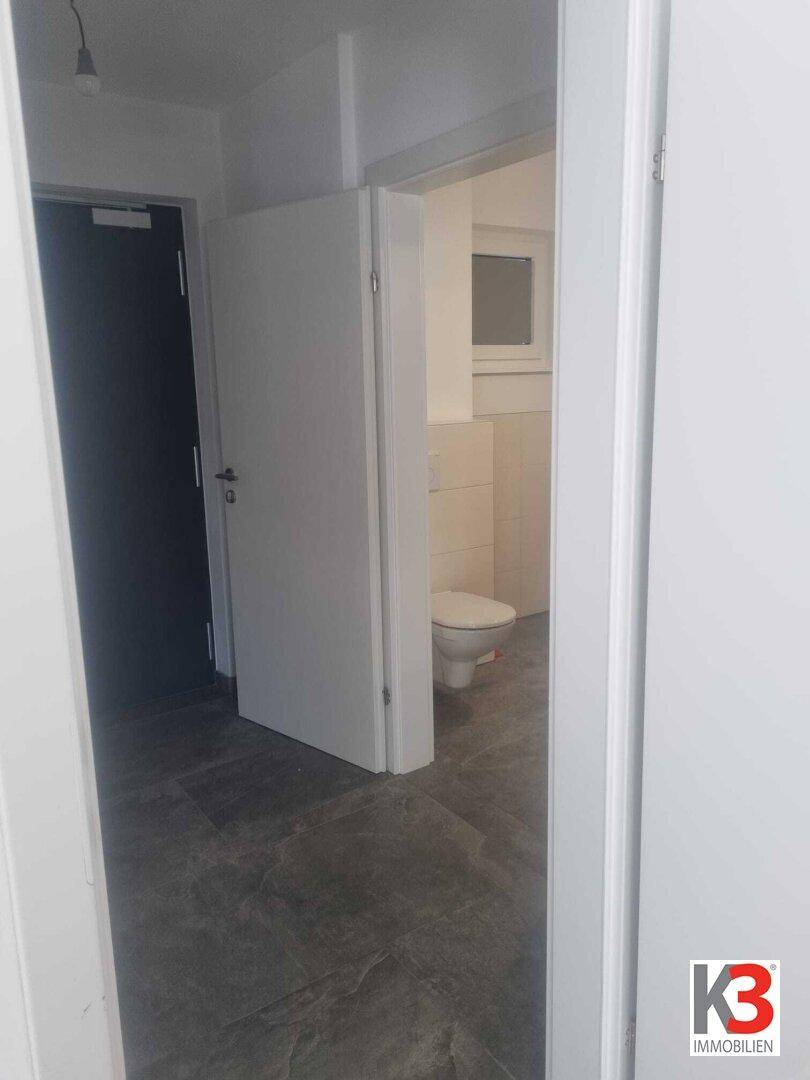Heller Flur mit Fliesenboden und Zugang zu einem Badezimmer mit WC.