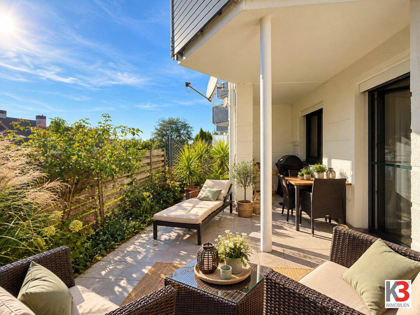 Sonnige Terrasse mit bequemen Gartenmöbeln und Essbereich, umgeben von grüner Bepflanzung.