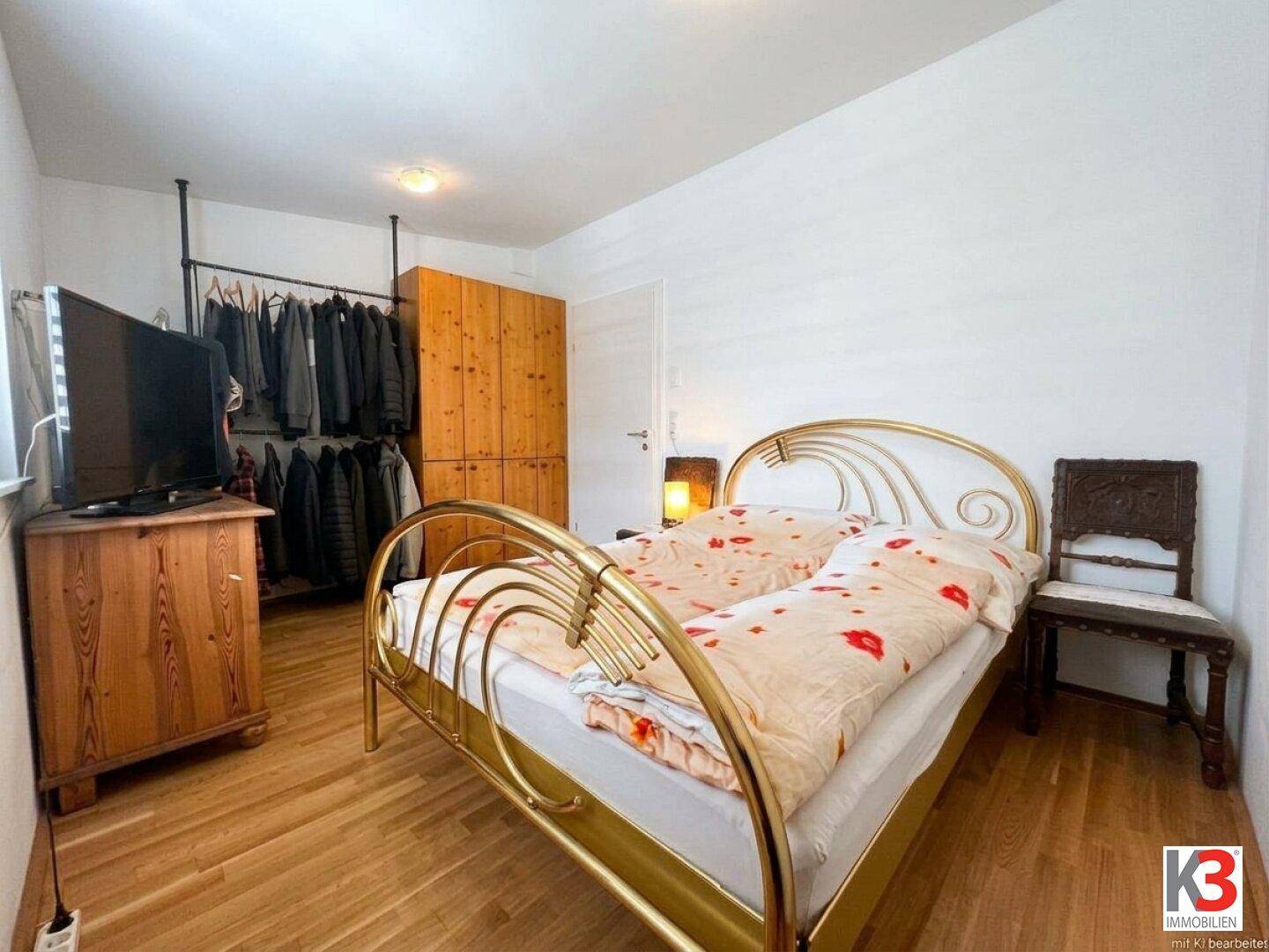 Schlafzimmer mit Doppelbett, Holzfußboden und einem offenen Kleiderständer sowie Holzschrank.