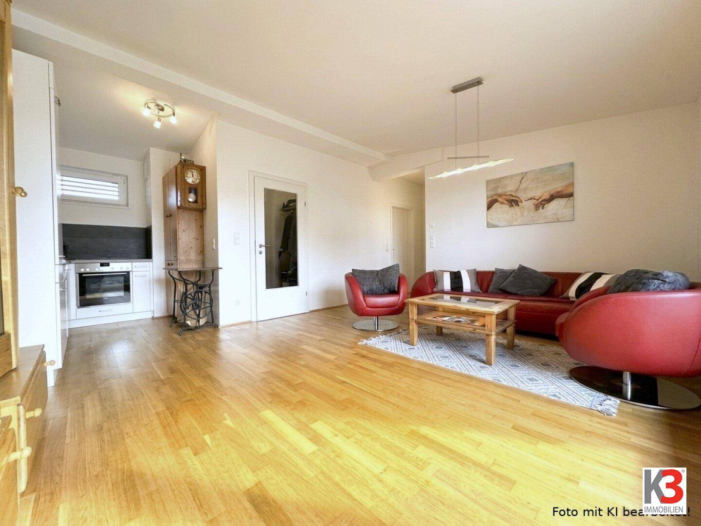 Heller Wohnbereich mit Holzboden, rotem Sofa und einer kleinen, integrierten Küchenzeile.