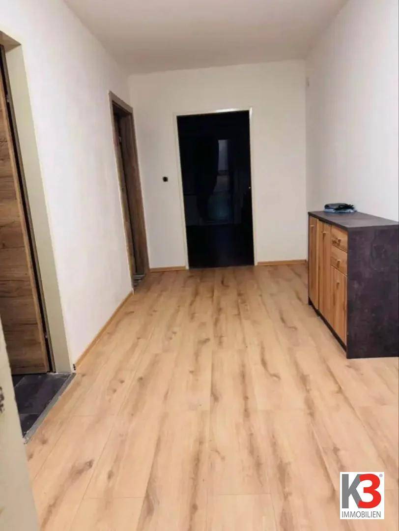 Heller Flur mit Holzboden und einer kleinen Kommode, der zu weiteren Räumen führt.