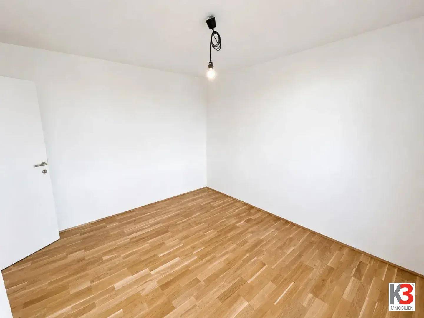 Leeres Zimmer mit hellem Fischgrätparkettboden und weißen Wänden, ideal als Schlaf- oder Arbeitszimmer.