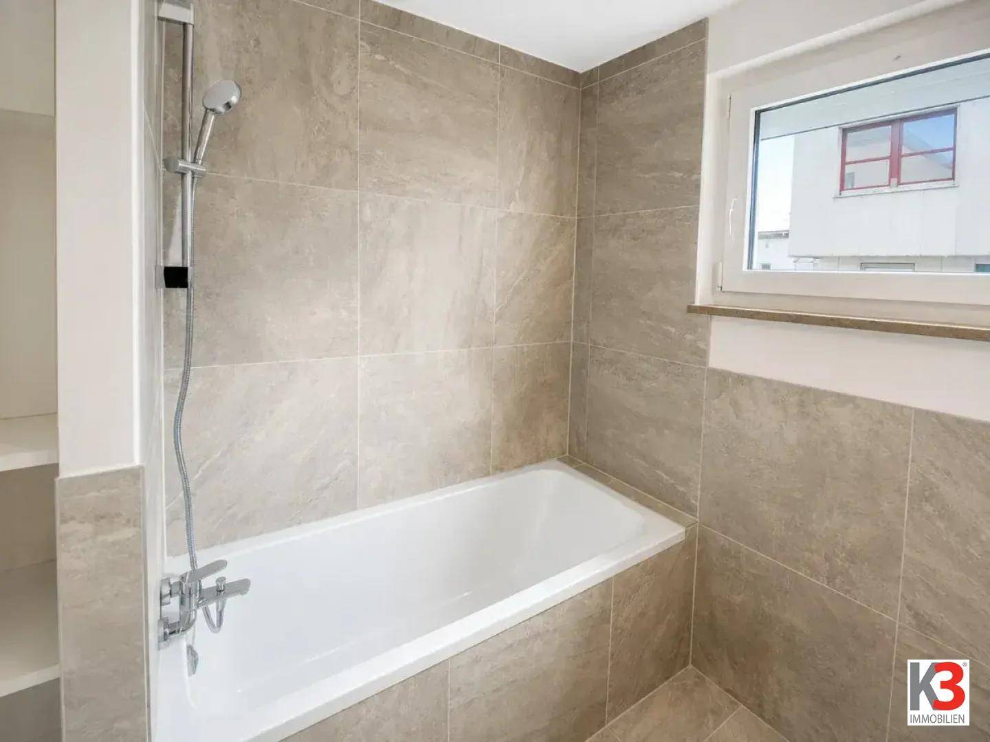 Badezimmer mit Badewanne, Duschfunktion und beigefarbenen Fliesen, inklusive Fenster für Tageslicht.