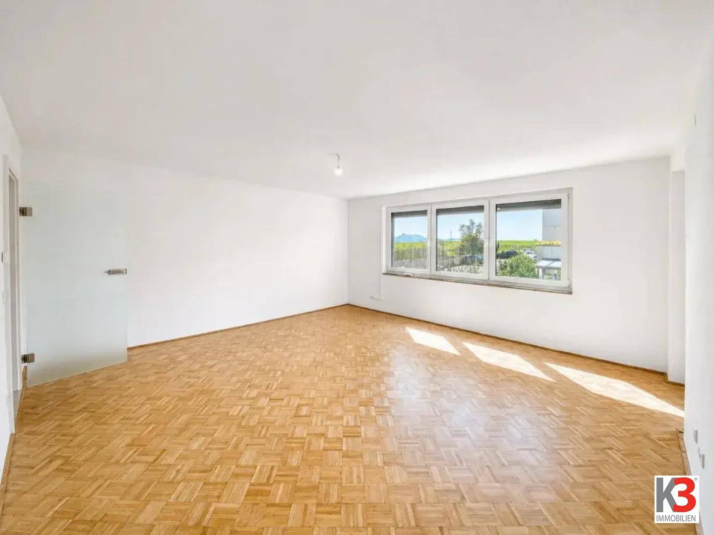 Helles Wohnzimmer mit Fischgrätparkett und weitem Blick ins Grüne durch große Fenster.