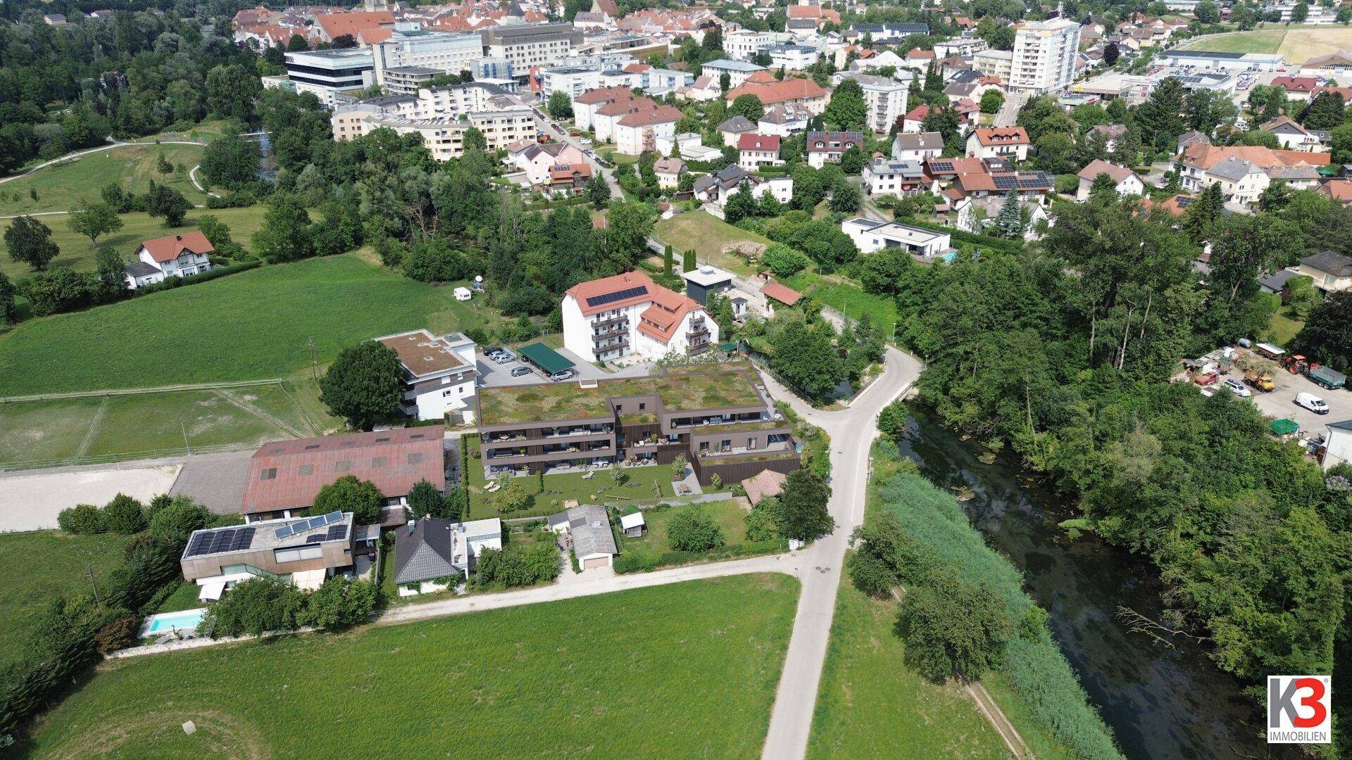 Luftaufnahme des Wohnkomplexes in einer grünen Umgebung mit angrenzender städtischer Bebauung.
