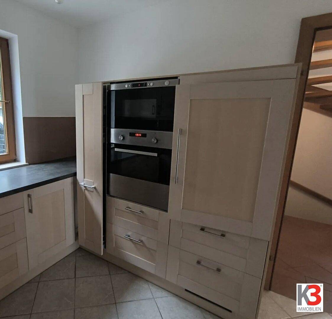 Integrierte Küchengeräte wie Backofen und Mikrowelle in den hellen Holzschränken.