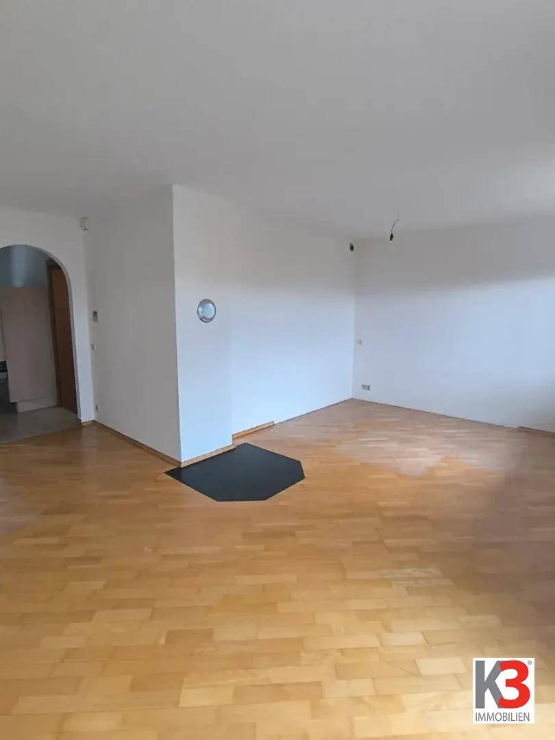 Geräumiges Wohnzimmer mit hellem Parkettboden und weißen Wänden, unmöbliert.