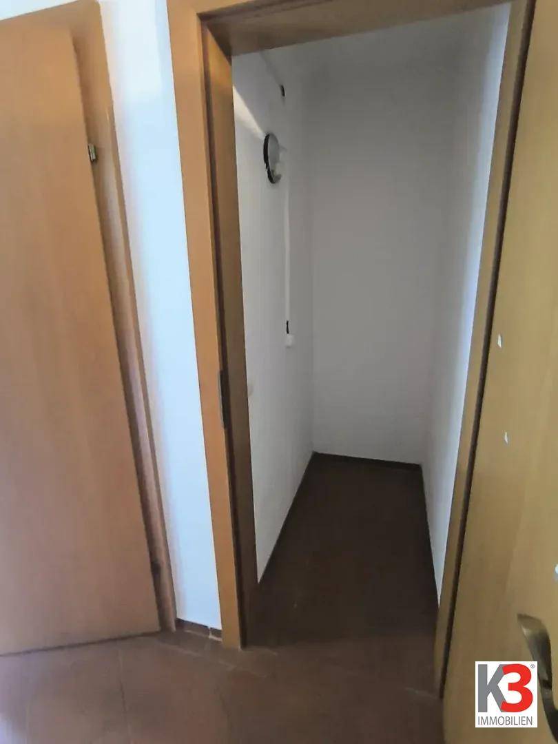 Kleiner, praktischer Abstellraum mit weißen Wänden und dunklem Fliesenboden.