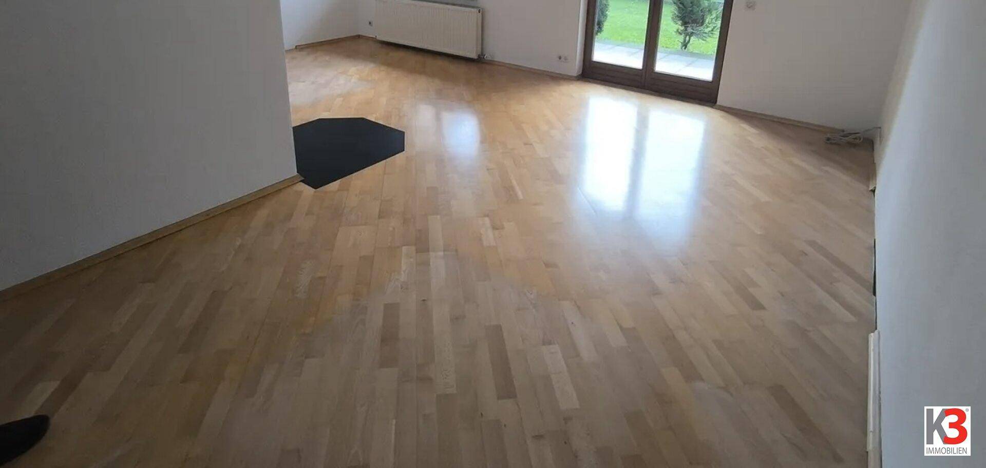 Heller Wohnbereich mit glänzendem Parkettboden und Zugang zu einem Außenbereich.