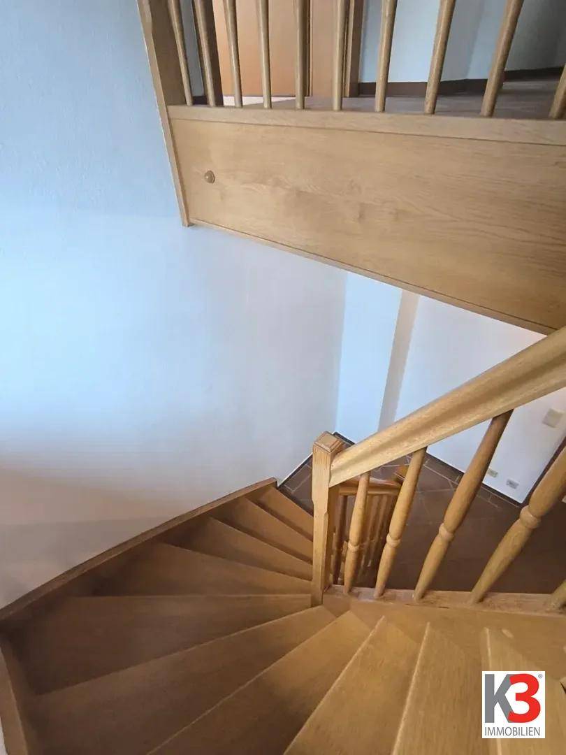 Helle Holztreppe mit Geländer führt in die obere Etage, gut beleuchtet.