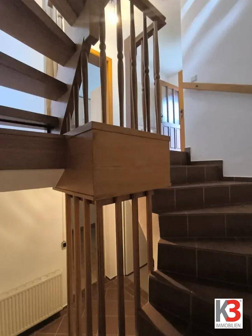 Treppenhaus mit Holzgeländer und gefliesten Stufen, führt zu weiteren Räumen.