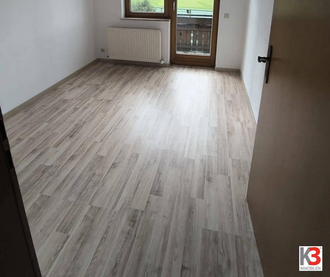 Helles Schlafzimmer mit Laminatboden und Zugang zu einem Balkon oder einer Loggia.