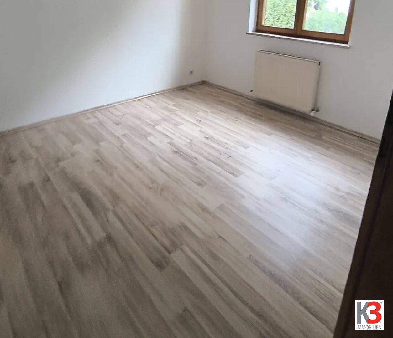 Schlafzimmer mit hellem Laminatboden, weiß gestrichenen Wänden und Fenster.