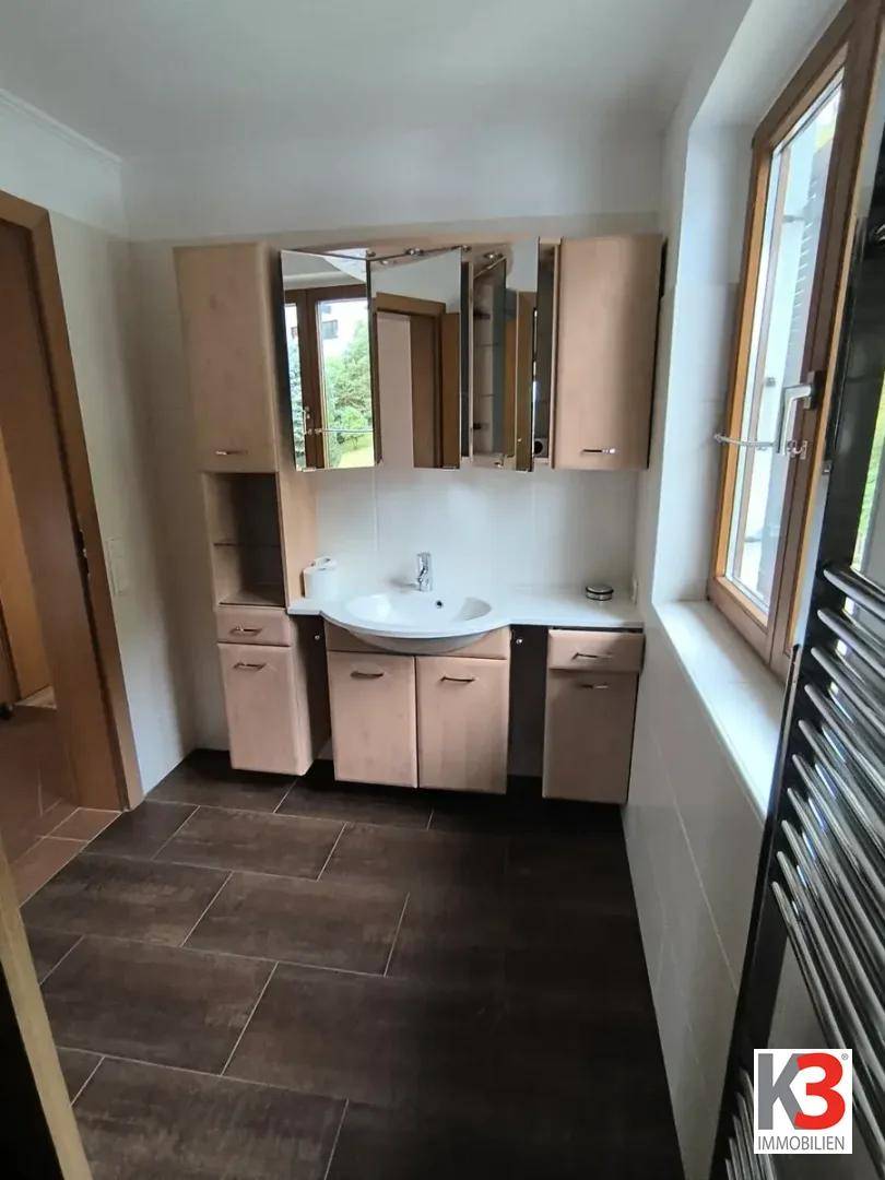 Badezimmer mit Waschtisch, Spiegelschrank und Fenster, in hellen Holztönen.