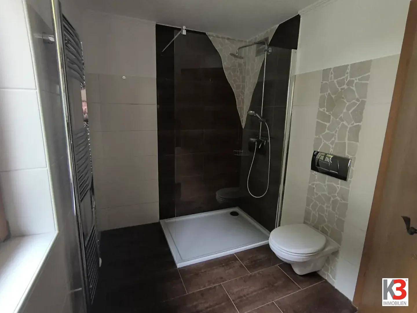 Modernes Badezimmer mit ebenerdiger Dusche, Wand-WC und beheiztem Handtuchhalter.