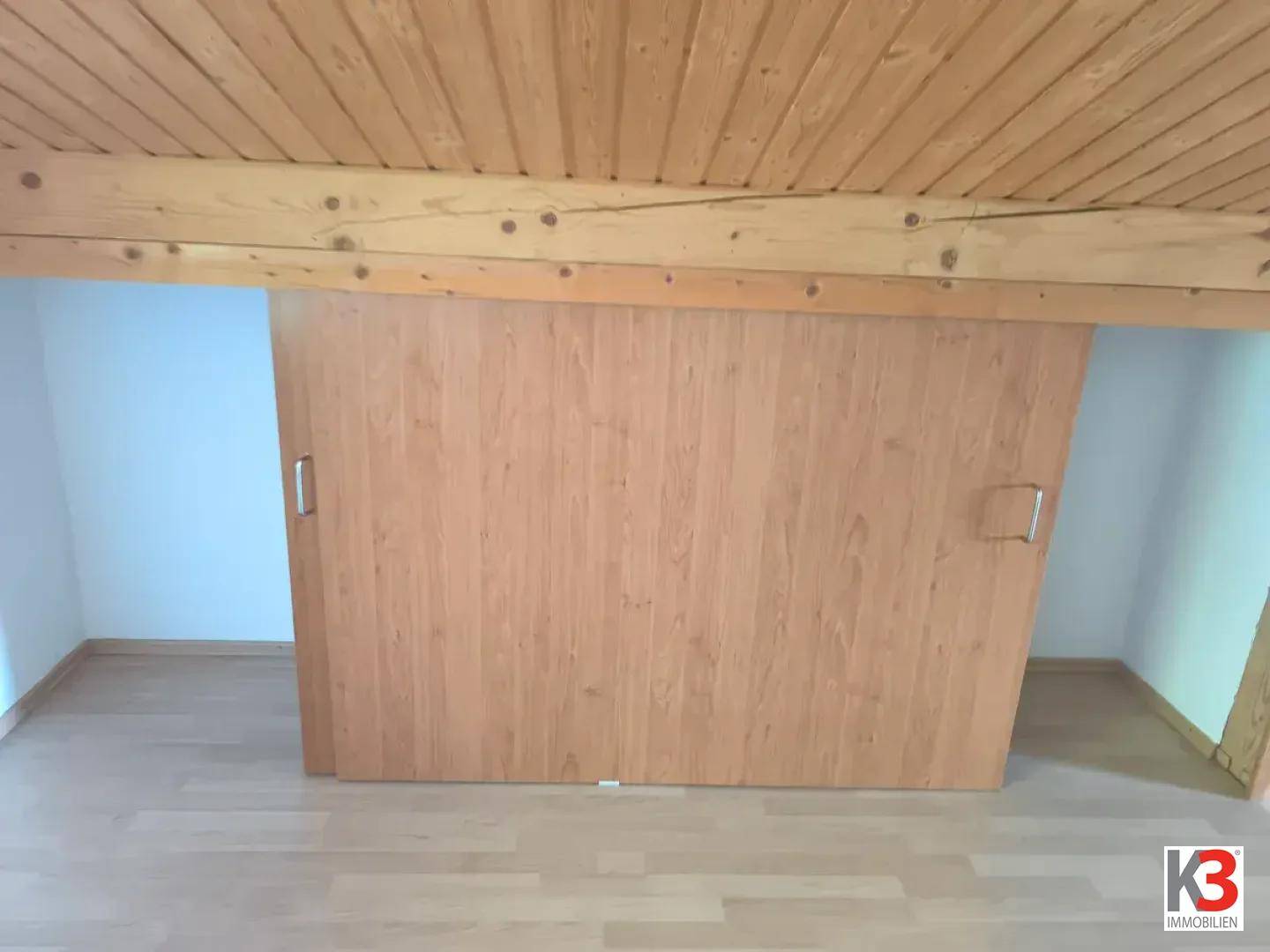 Dachbodenbereich mit Holzbalkendecke und integrierten Holzschiebetüren für Stauraum.