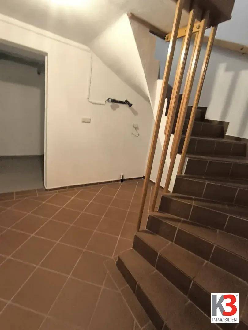 Treppenhaus mit gefliestem Boden und Holzgeländer, führt in den Kellerbereich.