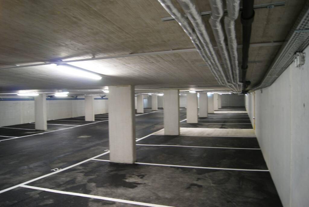 Geräumige Tiefgarage mit vielen markierten Stellplätzen, Betonpfeilern und sichtbaren Installationen an der Decke.