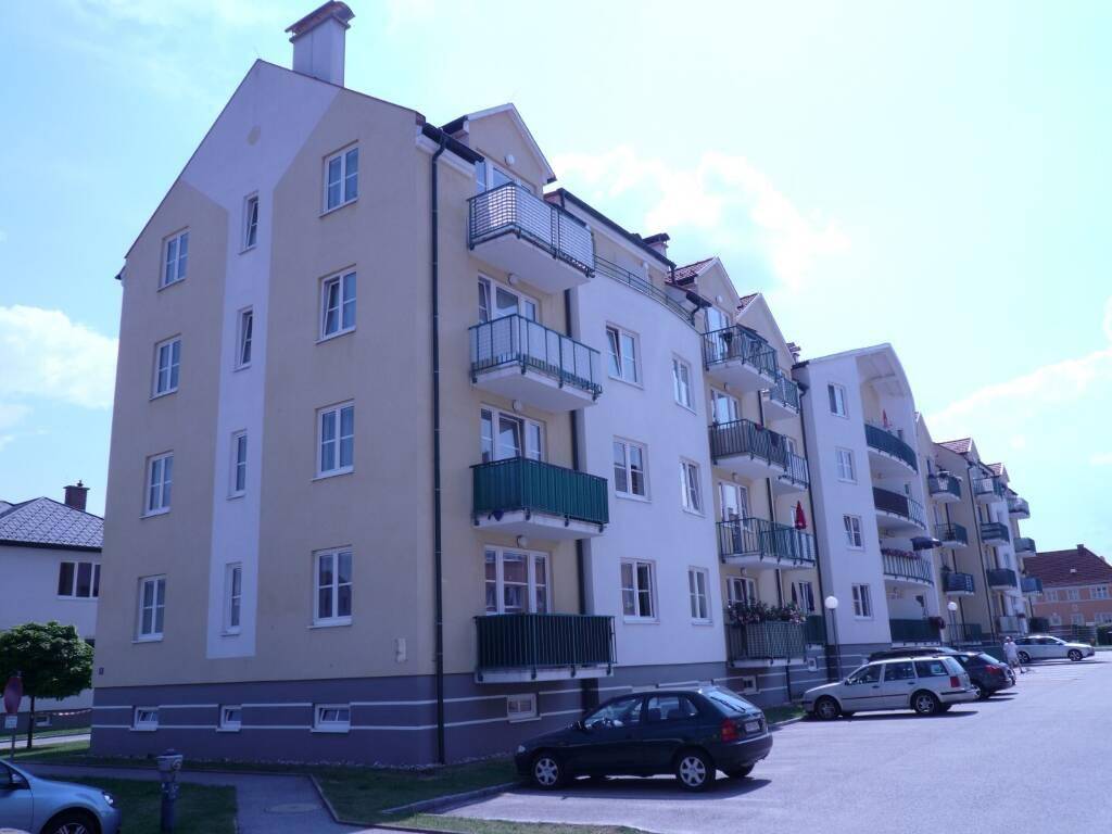 Mehrfamilienhaus mit hellbeiger Fassade, weißen Fenstern und Balkonen unter blauem Himmel.