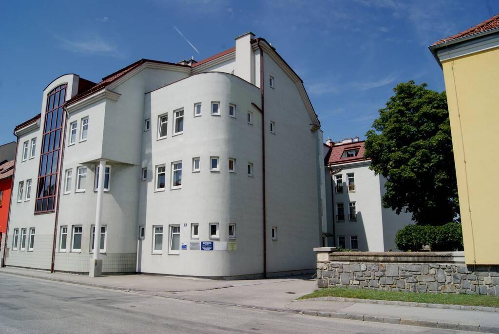 Modernes Gebäude mit heller, geschwungener Fassade, vielen Fenstern und einem markanten vertikalen Glasbereich an der Straßenecke.