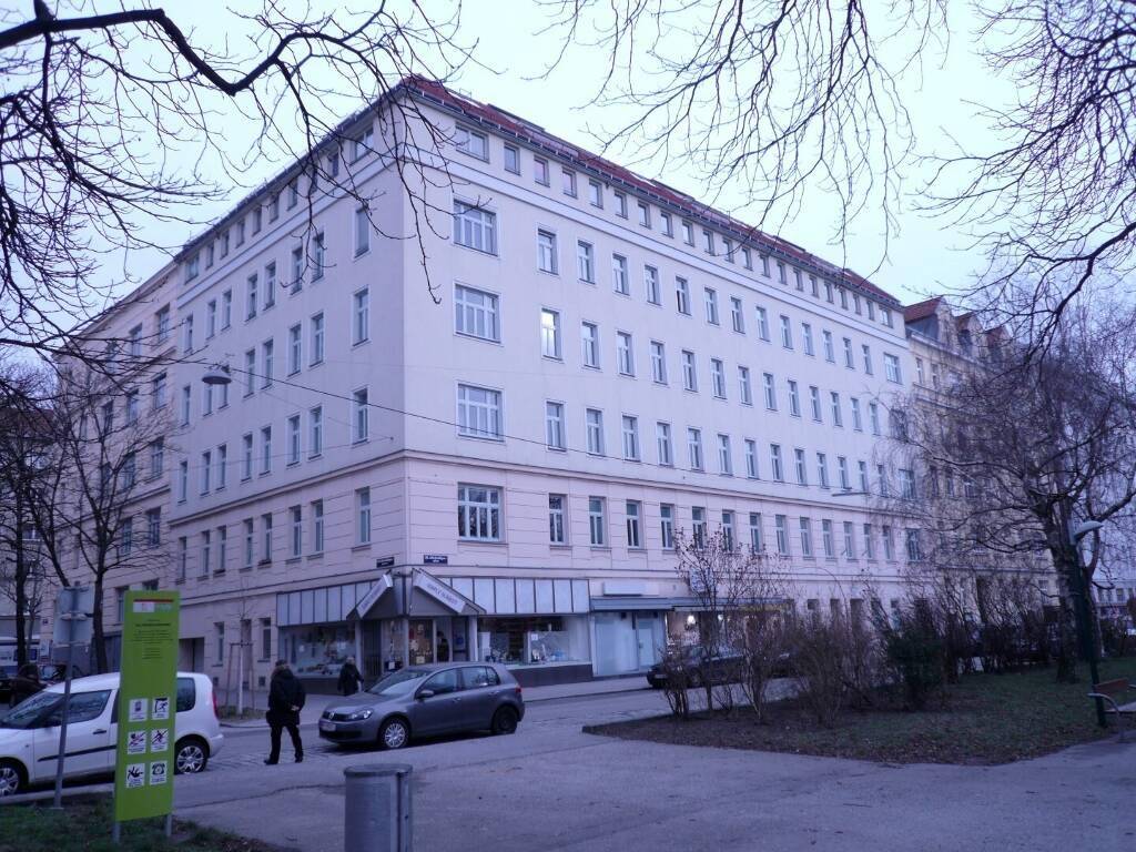 Eckgebäude mit mehreren Etagen und Geschäften im Erdgeschoss an einem trüben Tag in der Stadt.