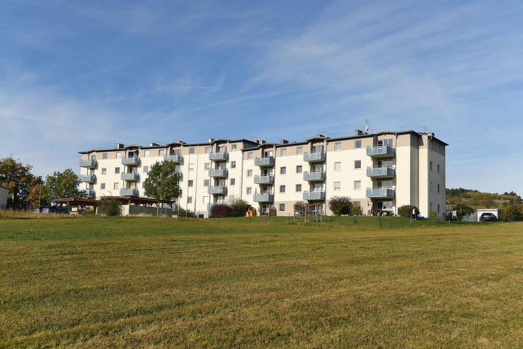 Wohngebäude mit Balkonen, umgeben von weiten Grünflächen unter einem klaren, blauen Himmel.