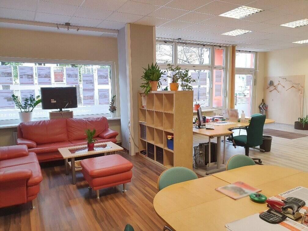 Geräumiger Bürobereich mit bequemer Sitzecke, mehreren Arbeitsplätzen und großen Schaufenstern.