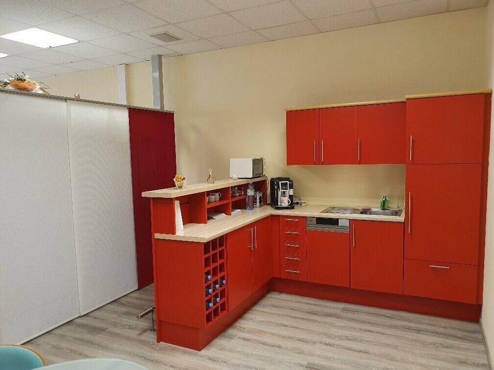 Funktionale Küchenzeile mit roten Schränken, Mikrowelle, Kaffeemaschine und integriertem Weinregal.